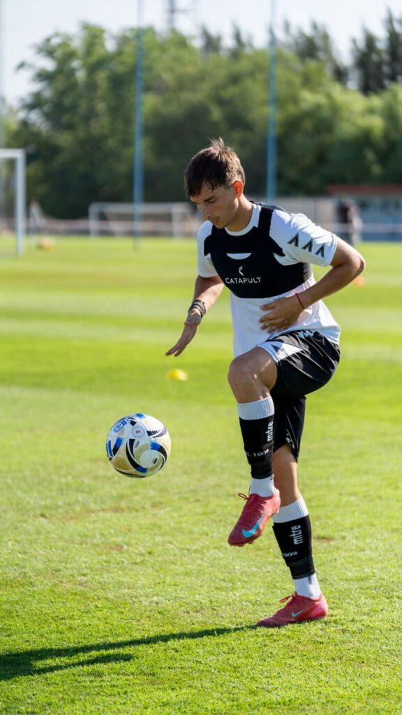 A young male athlete practicing soccer on a sunny day outdoors on a green field.