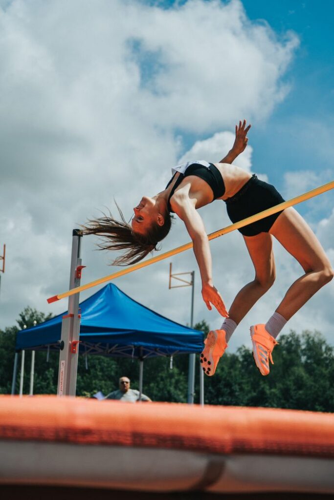 Dynamic shot of a female athlete clearing the bar during a high jump event outside.